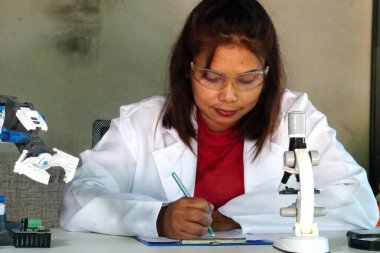 Asyalı kadın mikroskopla kapalı alanda araştırma yapıyor..