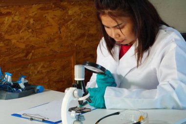 Asyalı kadın mikroskopla kapalı alanda araştırma yapıyor..