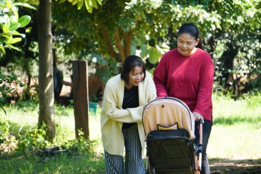 İki kadın bebek arabasının yanında durur ve gülümseyerek bebeğe bakar..