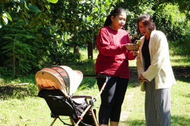 İki Asyalı kadın ellerinde telefonla bebek arabasının yanında duruyor.