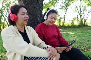 Bahçede dinlenirken tabletli iki Asyalı kadın
