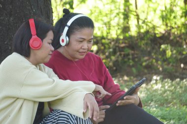 Bahçede dinlenirken tabletli iki Asyalı kadın
