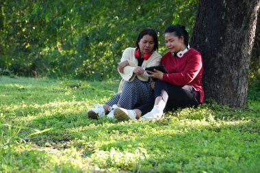 Tabletle ağacın altında çimenlerde yan yana oturan iki kadın.