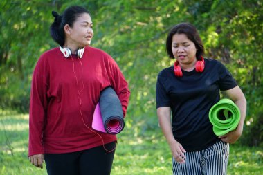 Parkta yoga minderleriyle yürüyen iki kadın.