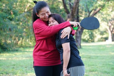 Pickleball oynadıktan sonra iki kadın parkta sevgiyle kucaklaşıyor..