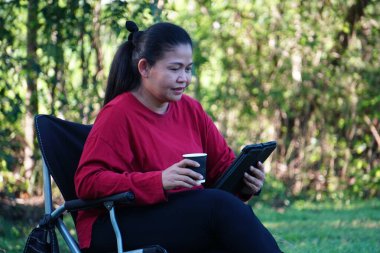 Tablet kullanarak sandalyede oturan Asyalı kadın..