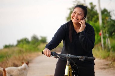 Ormanda bisikleti ve cep telefonu olan Asyalı bir kadın.