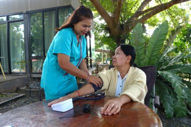 Yaşlı bir kadının kalp atışlarını kontrol etmek için steteskop kullanan bir hemşire..