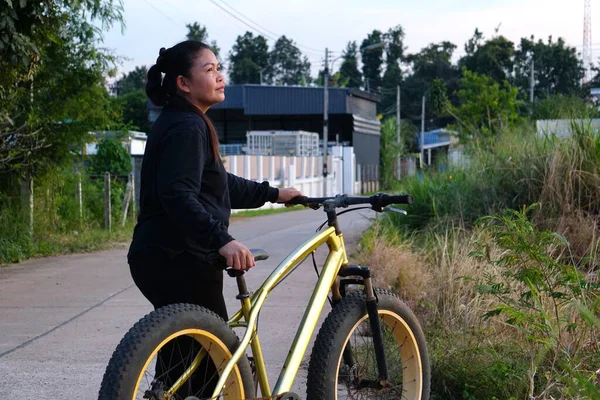 Asyalı bir kadın toprak yolda dağ bisikletine mola veriyor, gerçekten ileriye bakıyor..