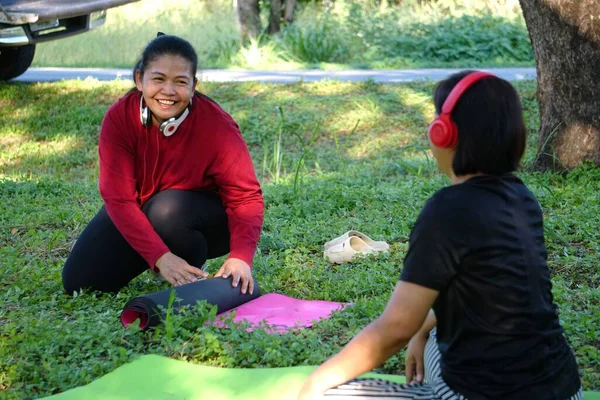 Çimenlerde oturmuş, yoga sonrası gülümseyen ve konuşan iki kadın.