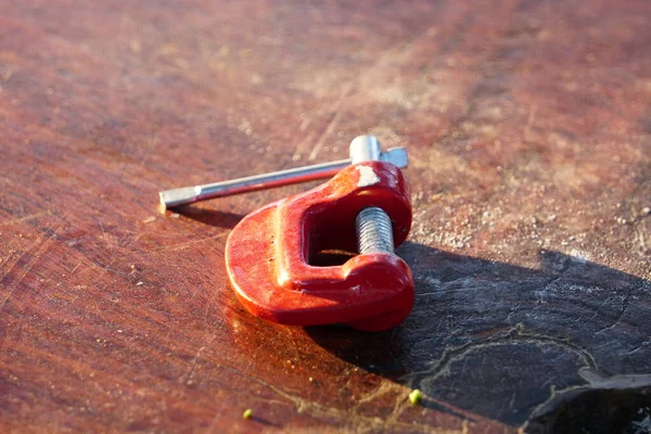 Tahta yüzeyde duran kırmızı klemp aracı.