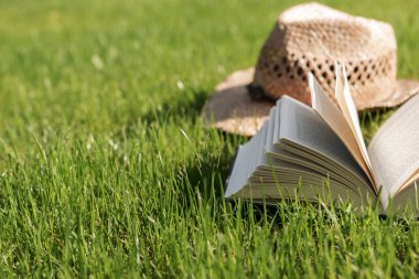 Açık bir kitap arka planda hasır şapkayla çimenlikte yatıyor. Koronavirüs salgını sırasında bahçede rahatlama