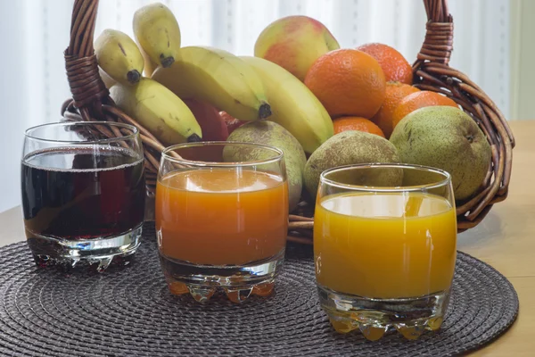 バック グラウンドでフルーツ バスケットとグラスの中のマルチ フルーツ柑橘類ジュース — ストック写真