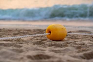 Okyanus dalgalarının yanındaki sahilde bulunan iplere bağlı sarı şamandıraya yakın. 