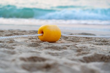 Okyanus dalgalarının yanındaki sahilde bulunan iplere bağlı sarı şamandıraya yakın. 