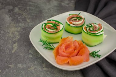 Salatalıklı füme somon ve beyaz tabakta yumuşak peynirli rulo.