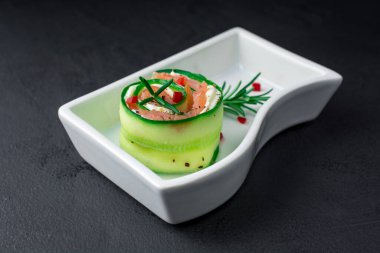 Salatalıklı füme somon ve beyaz tabakta yumuşak peynirli rulo.