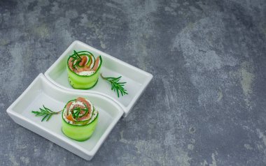 Salatalıklı füme somon ve beyaz tabakta yumuşak peynirli rulo.