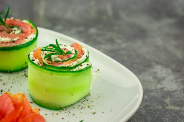 Salatalıklı füme somon ve beyaz tabakta yumuşak peynirli rulo.