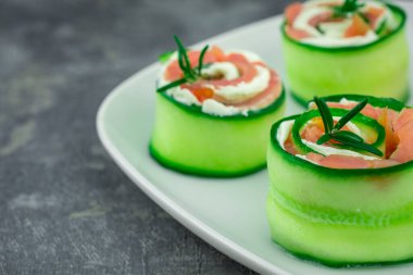 Salatalıklı füme somon ve beyaz tabakta yumuşak peynirli rulo.