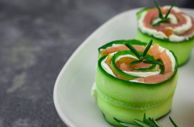 Salatalıklı füme somon ve beyaz tabakta yumuşak peynirli rulo.