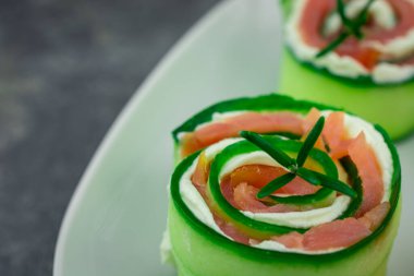 Salatalıklı füme somon ve beyaz tabakta yumuşak peynirli rulo.