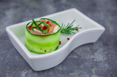 Salatalıklı füme somon ve beyaz tabakta yumuşak peynirli rulo.