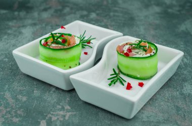 Salatalıklı füme somon ve beyaz tabakta yumuşak peynirli rulo.