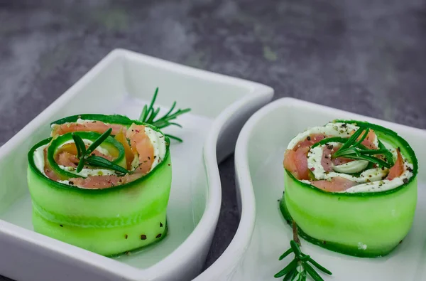 Salatalıklı füme somon ve beyaz tabakta yumuşak peynirli rulo.