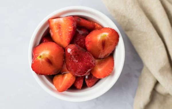 Yukarıdan beyaz bir masada kasede çilek.
