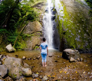 Asyalı kadın şelalenin altında tek başına duruyor. Doğada tek başına seyahat etmek.