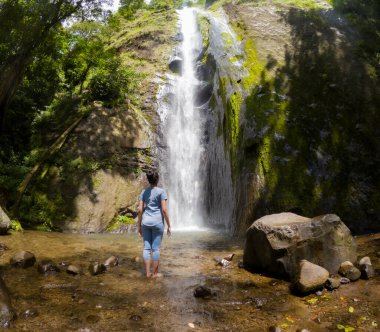 Asyalı kadın şelalenin altında tek başına duruyor. Doğada tek başına seyahat etmek.