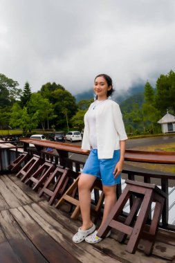 Arka planda orman ve dağlar olan bir yiyecek standında tek başına duran Asyalı bir kadın. Tek başına seyahat ve aşçılık.