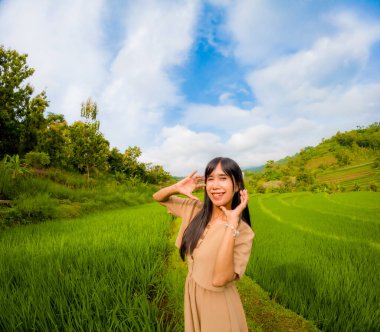 Asyalı bir kadın tek başına gezmekten zevk alıyor. Mutlu görünüyor ve pirinç tarlalarının atmosferinin tadını çıkarıyor..