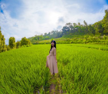 Asyalı bir kadın tek başına gezmekten zevk alıyor. Mutlu görünüyor ve pirinç tarlalarının atmosferinin tadını çıkarıyor..