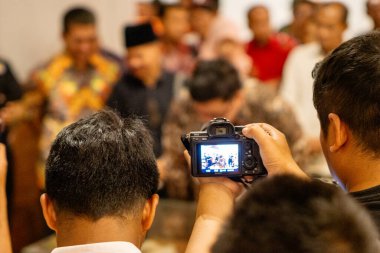 Asyalı bir gazeteci haber toplamak için bir etkinlik kaydediyor. Olayı kaydetmeye odaklan.