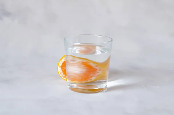 Цитрусовые мандарина отражаются через стеклянную чашку с водой на сером фоне. Искаженное изображение воды. Арт концепция. Минимализм. Принято. Абстракция. Перспективные, сломанные и искаженные изображения — стоковое фото