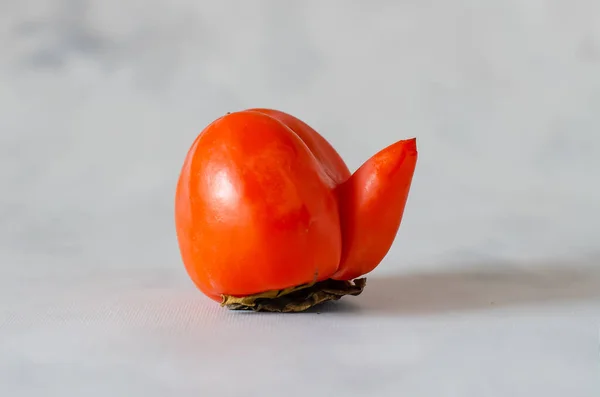 Una extraña forma de fruta. Feo caqui sobre un fondo gris. Dulce sabrosa fruta kaki. El concepto de alimentación saludable, vegano, dieta vegetariana. —  Fotos de Stock