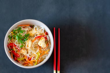 Cam erişteli Asya salatası, tavuk ve sebzeler havuç, dolma biber ve yemek çubuklarıyla birlikte gri bir tabakta susam tohumları. Düz yatıyordu. Yatay oryantasyon. Boşluğu kopyala.