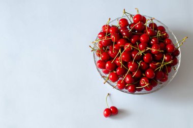 Olgun, taze kirazlar mavi arka planda cam bir kasede.