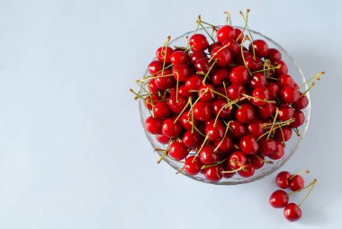 Olgun, taze kirazlar mavi arka planda cam bir kasede.