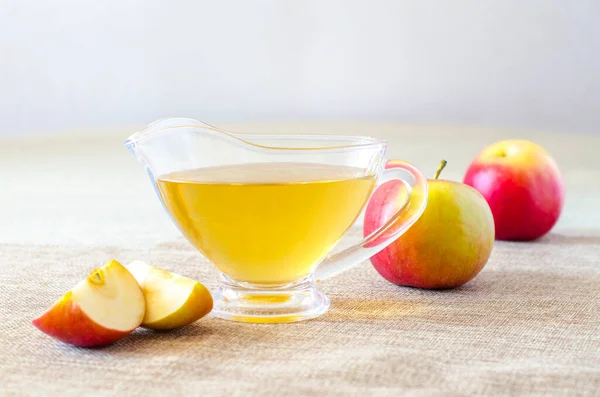 Glass gravy boat with apple cider vinegar and fresh fruits on a light wooden table. Close-up. — Stock Photo, Image