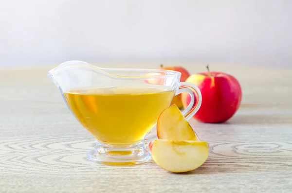 Apple cider vinegar in a glass gravy boat on a light background with red apples. Malic acid is beneficial for health and is used in cooking. — Stock Photo, Image