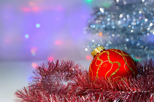 Red Christmas ball under the tree and tinsel — Stock Photo, Image