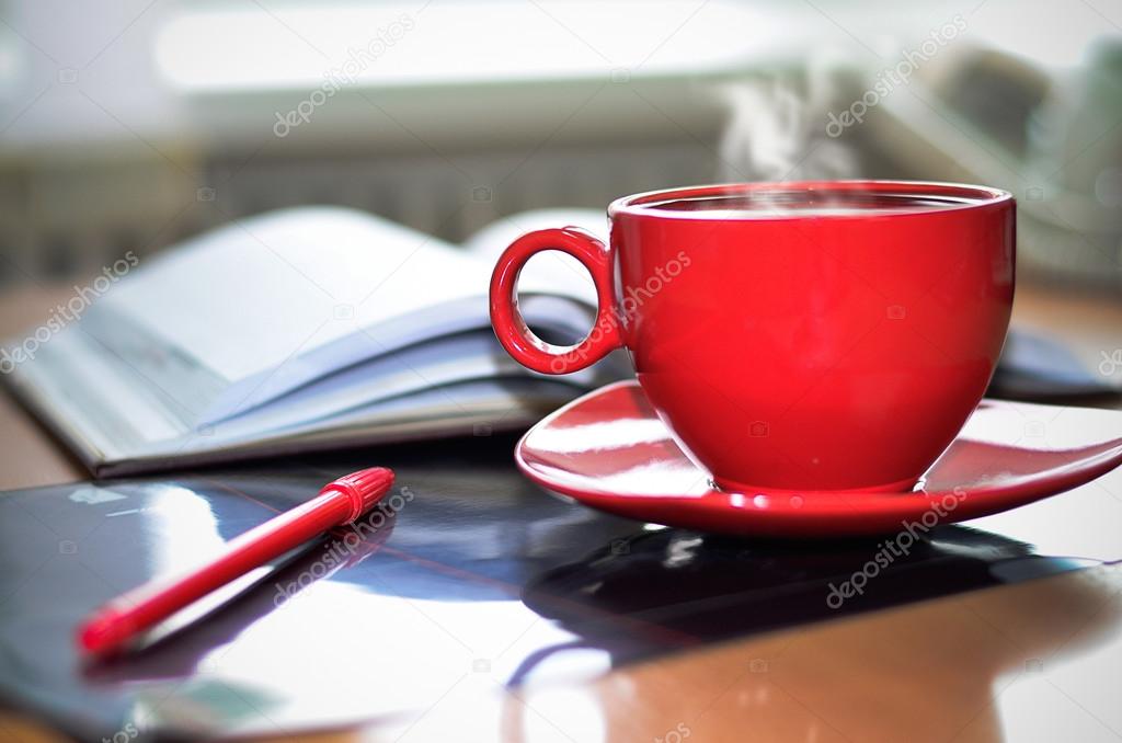 Red cup of hot coffee, notepad and pencil on the desktop
