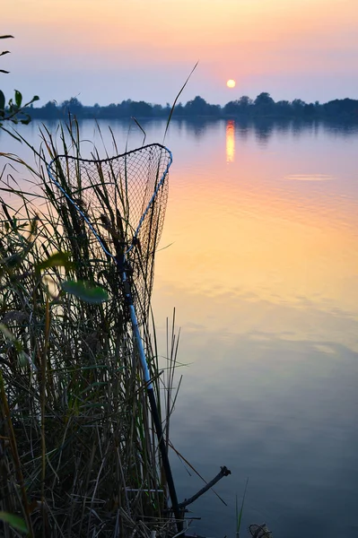 Рыболовный прут и аквариум против заката на озерной рыбалке — стоковое фото
