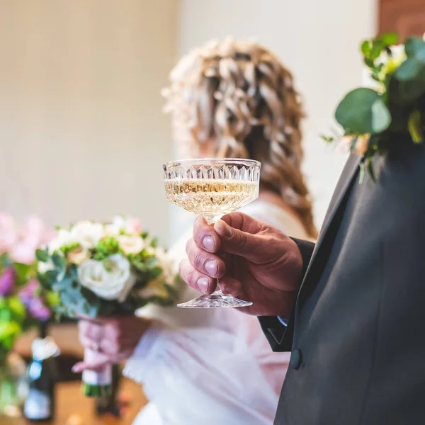 Damat elinde tutulan bir şampanya kadehinin yakın plan çekimi. Gelin arka planda hafifçe bulanıklaştı. Aşk, kutlama ve samimiyetle dolu romantik ve zarif bir düğün anını yakalıyor..