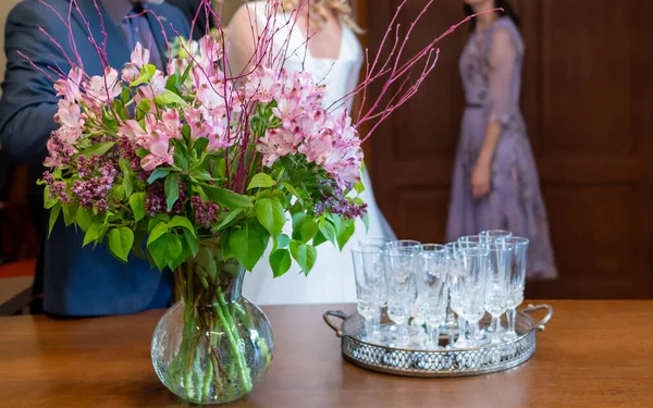 Özel bir durum için masası olan güzel dekore edilmiş bir kutlama salonu. Masanın üzerinde pembe çiçekli bir vazo duruyor, şampanya bardaklarıyla çevrili, zarif ve şenlikli bir atmosfer yaratıyor..