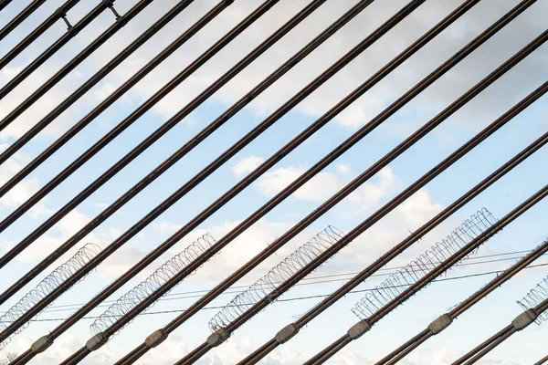 Metal kabloların yer aldığı sanatsal kompozisyon, parlak bir gökyüzü arka planına karşı tüm görüntüyü çapraz olarak genişletiyor. Minimalist perspektif ve geometrik çizgiler bir yapı, denge ve modern tasarım hissi yaratır..