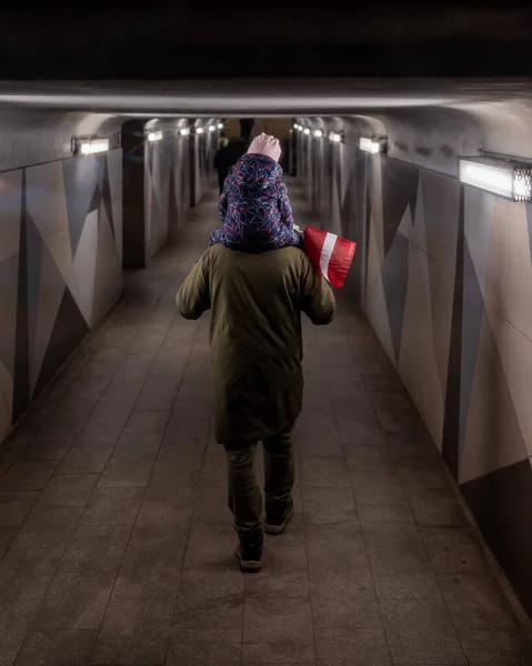 Omuzlarında küçük kırmızı beyaz bir bayrak taşıyan bir çocukla bir alt geçitten geçen bir adam. Loş bir yaya tünelinde arkadan vurulmuş..